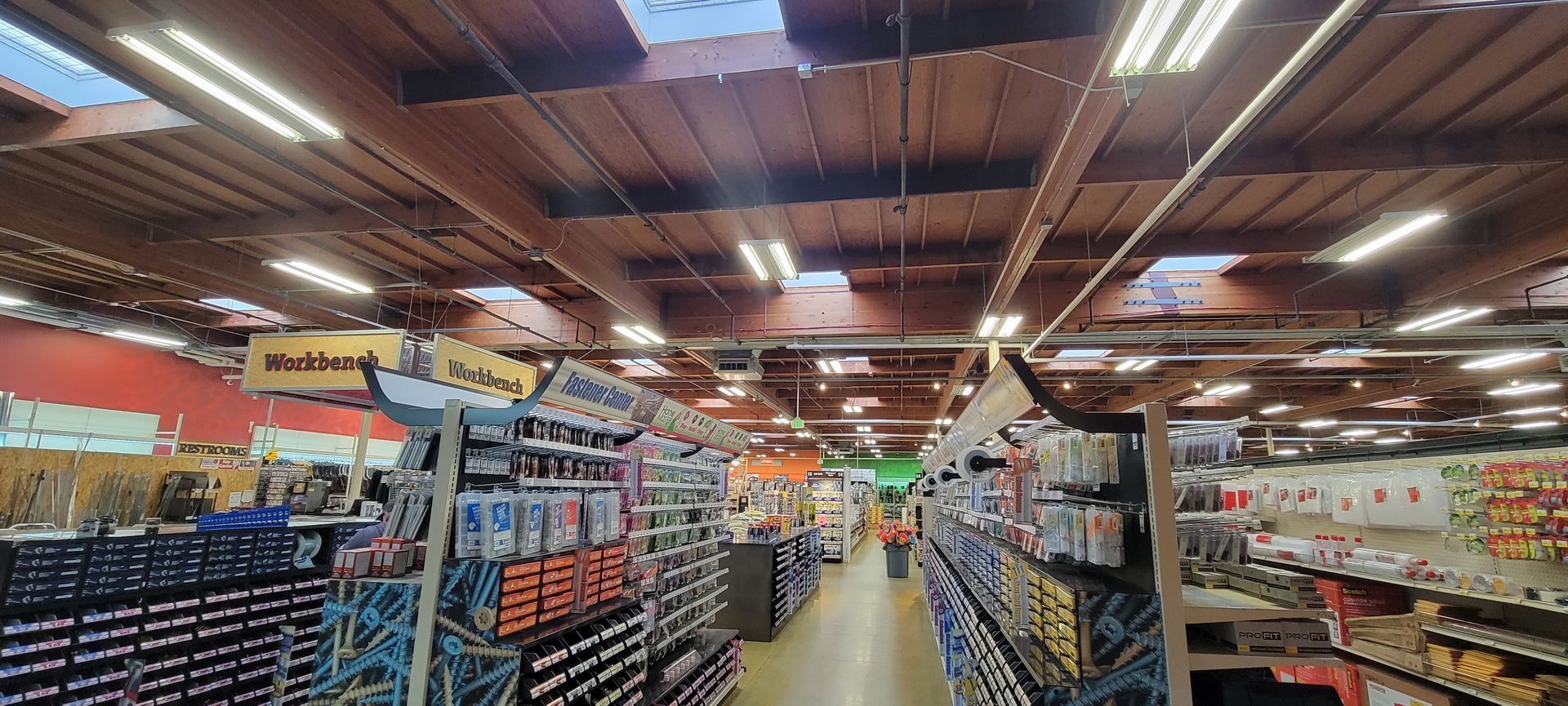 Aisles of a warehouse store with shelves of packaged goods under bright lights and a metal roof.