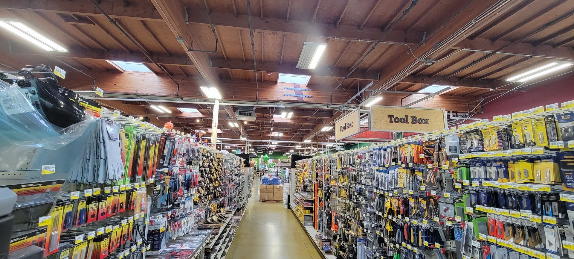 A hardware store aisle with tools and supplies on shelves under bright ceiling lights.
