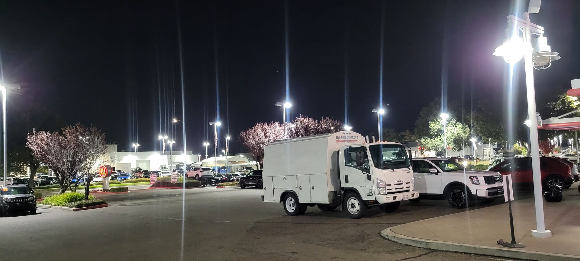 Nighttime parking lot with a white utility truck and bright streetlights outside stores