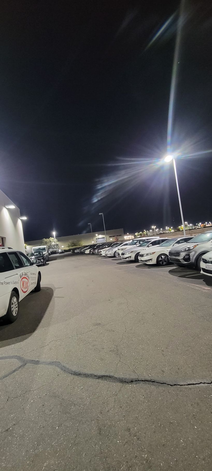 Nighttime parking lot with rows of parked cars and bright streetlights under a dark sky