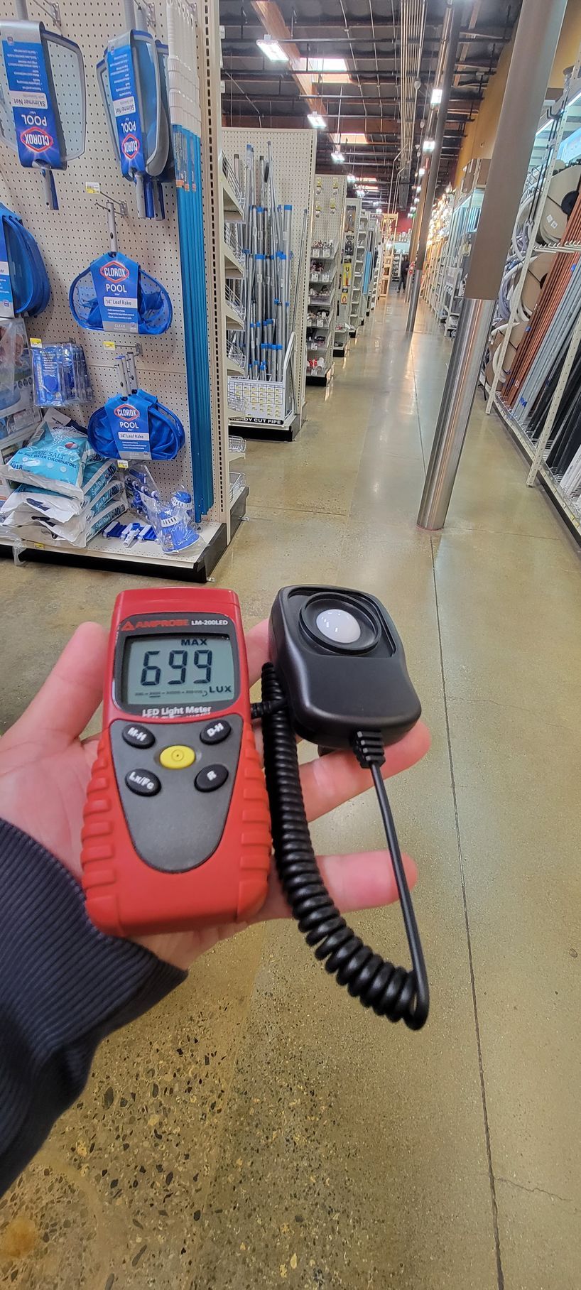 Handheld thermometer showing 69.9°F in a store aisle, with a probe on a coiled cable nearby