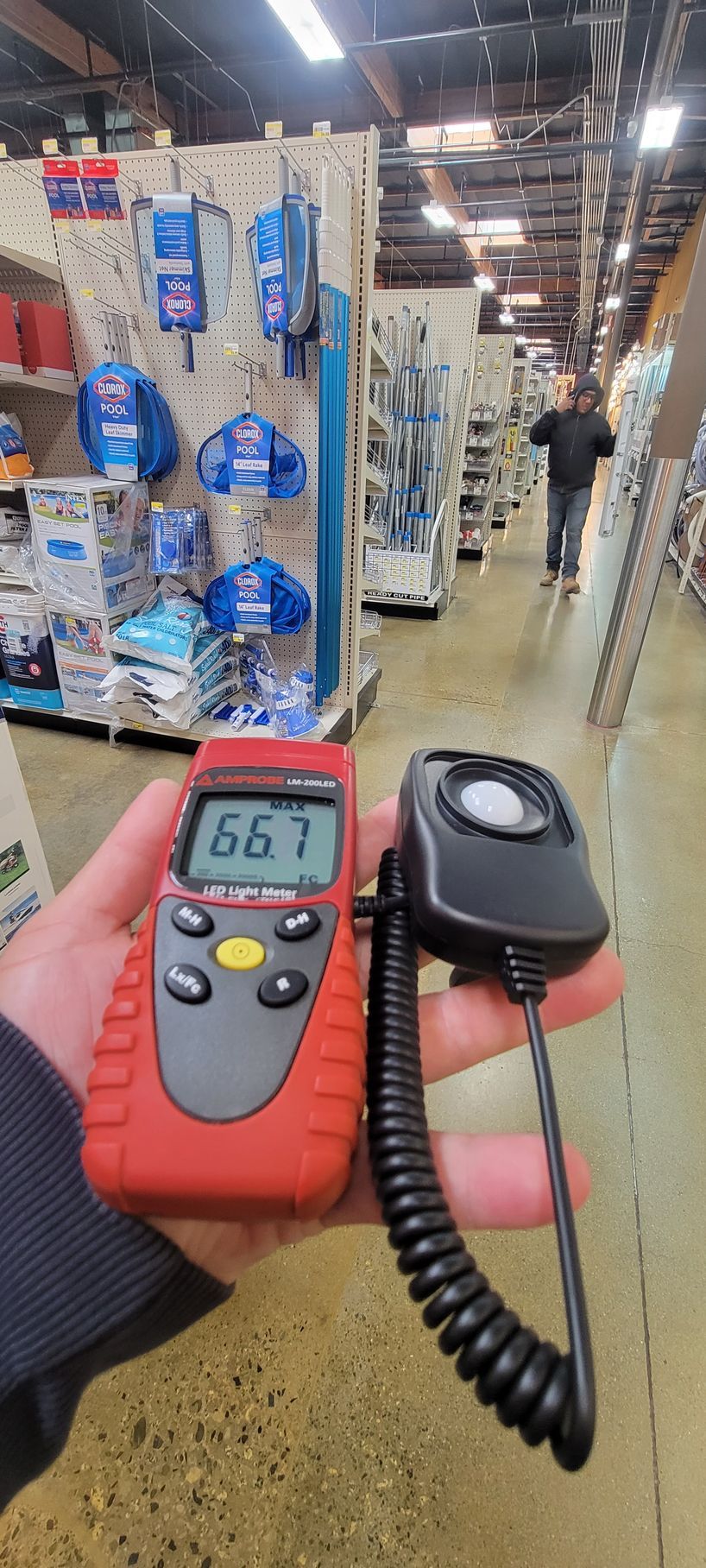 Handheld temperature meter with coiled probe in a store aisle, reading 66.7°F.