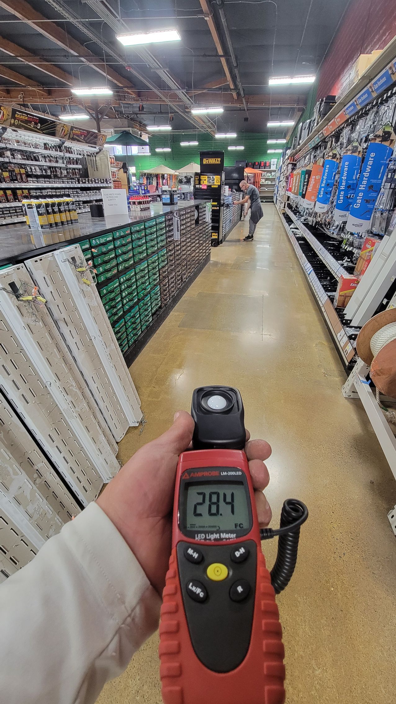 Handheld meter reading 28.4 in a hardware store aisle with shelves of tools and supplies