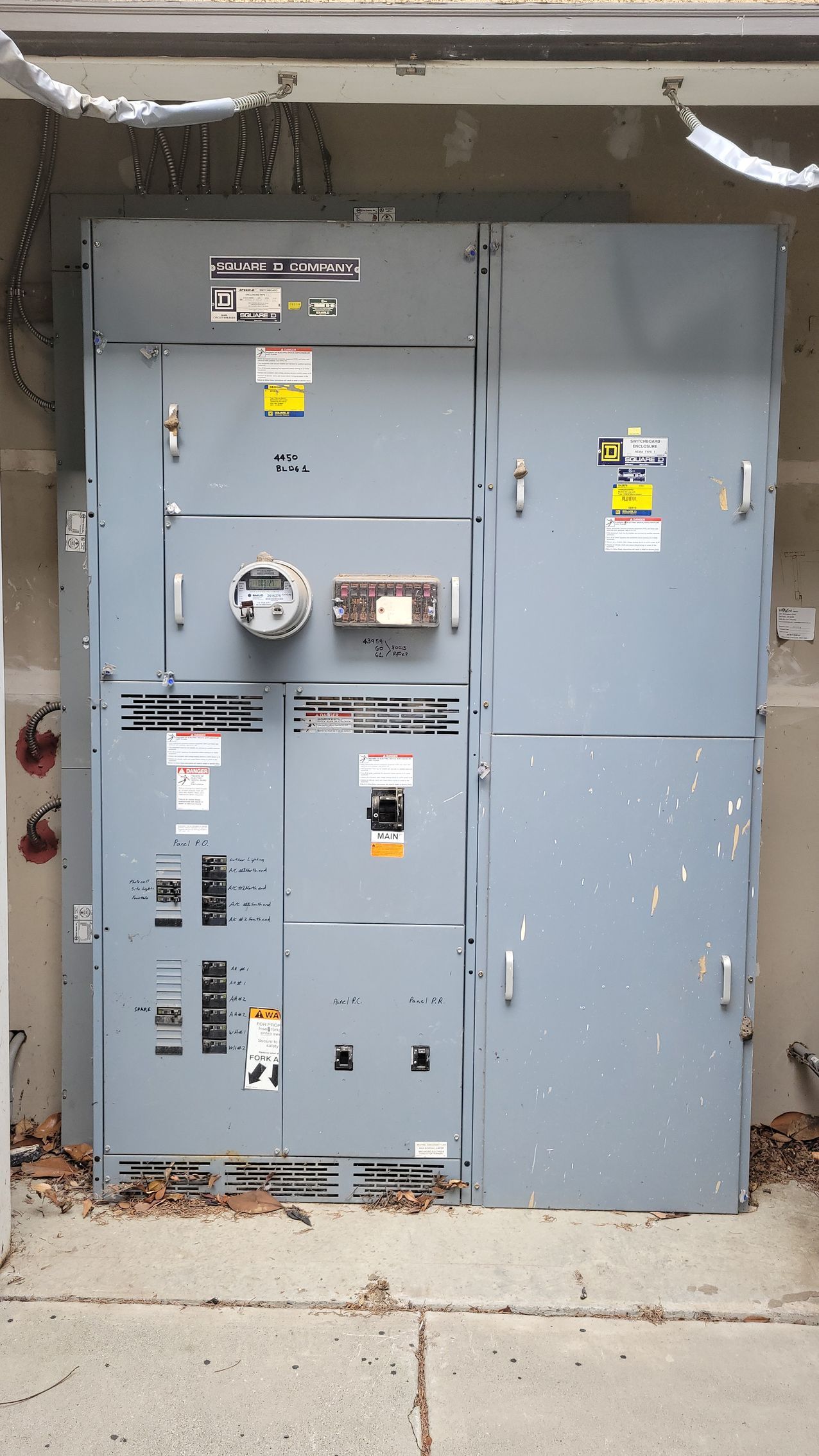 Gray utility electrical panels mounted on an outdoor wall beside a concrete walkway