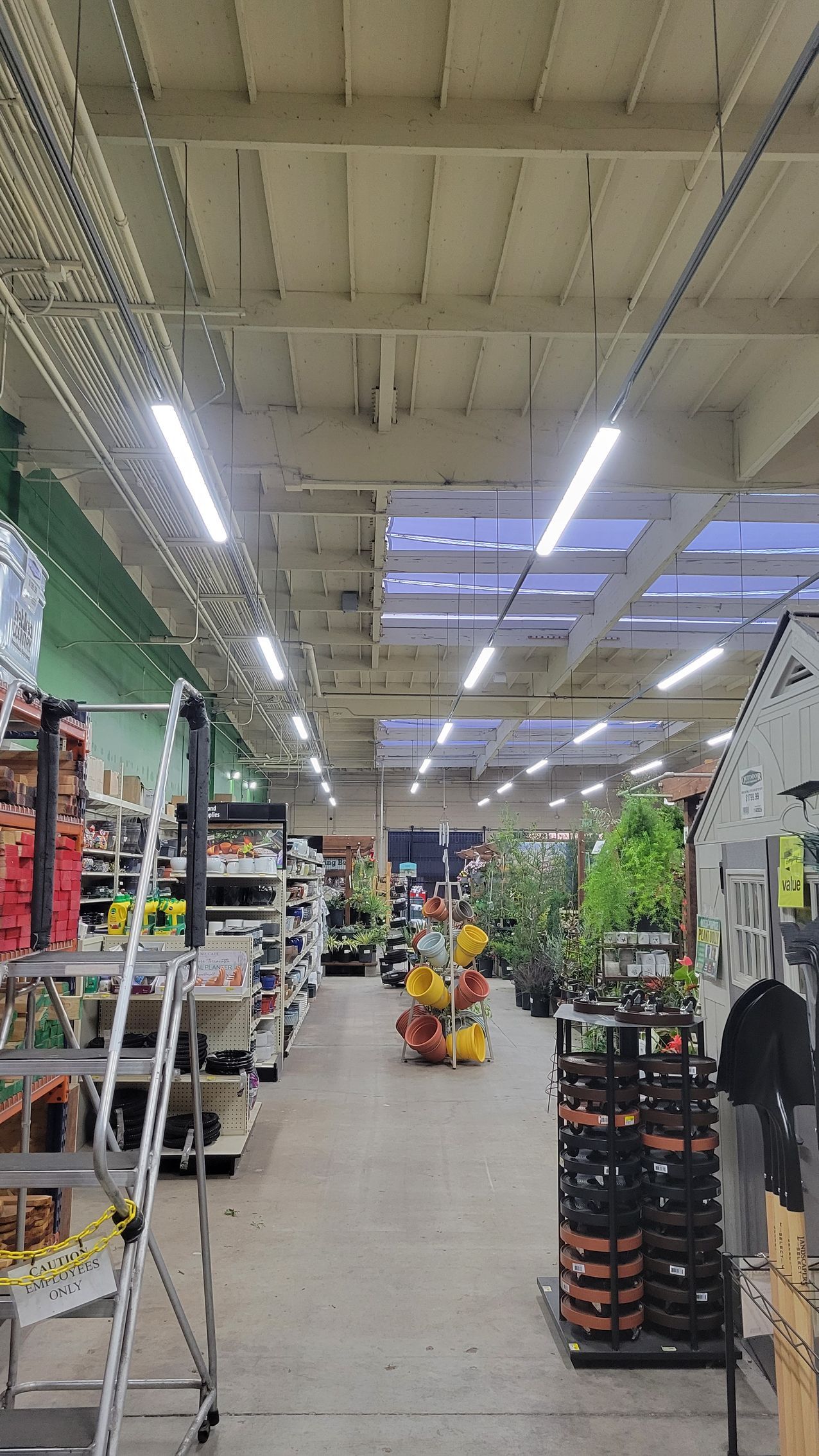 Garden center aisle with hanging lights, potted plants, and shelves of supplies in a store.