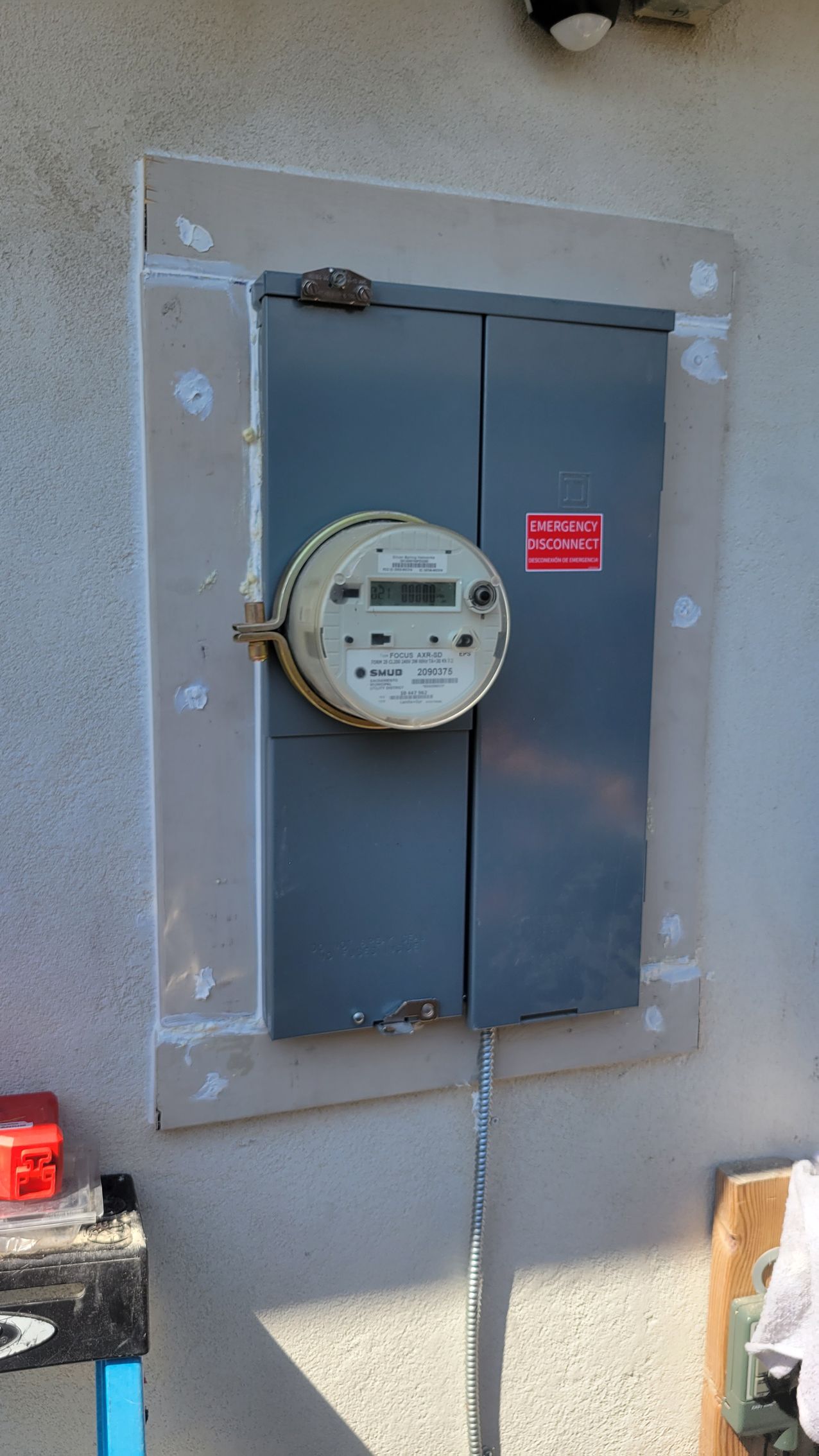 Electric meter mounted on a gray utility box on an exterior wall.