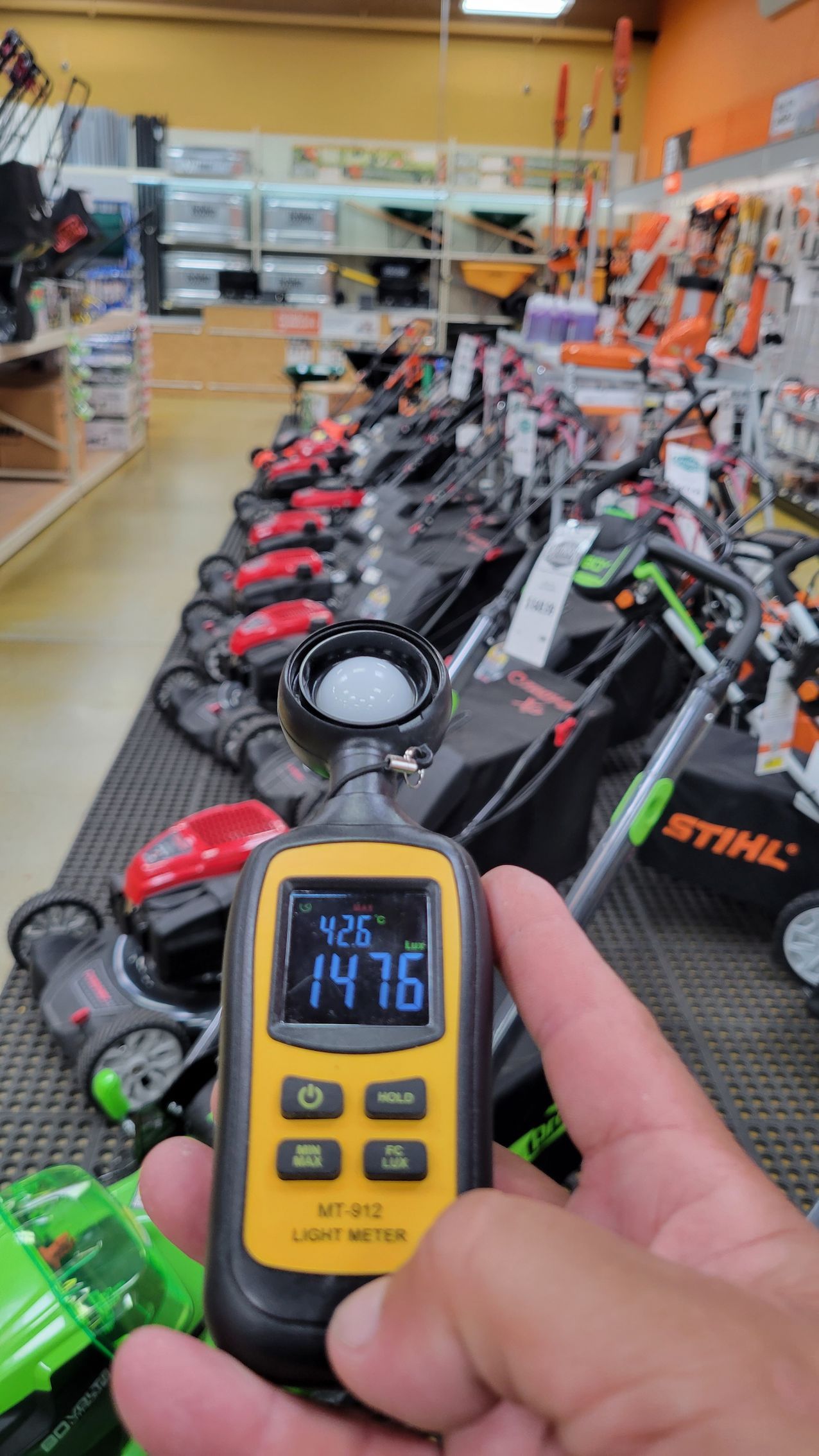Handheld meter reading 74.16 in a store aisle lined with Stihl power tools and equipment