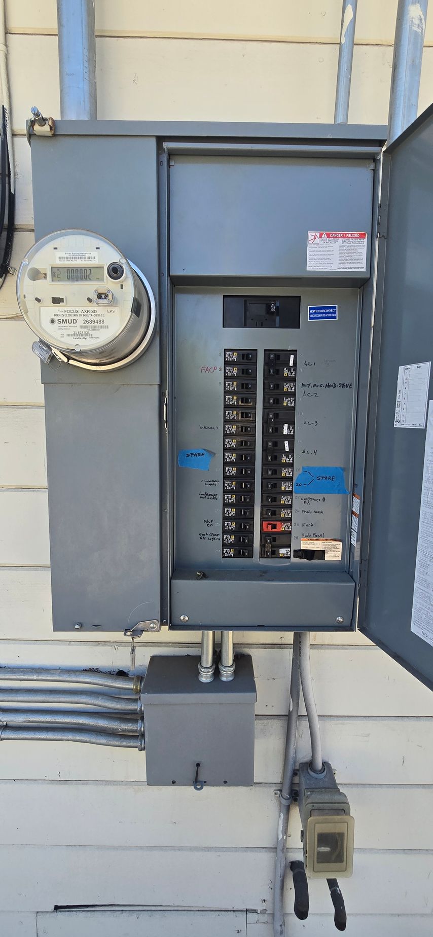 Open electrical breaker panel on a building exterior wall with utility meter beside it.