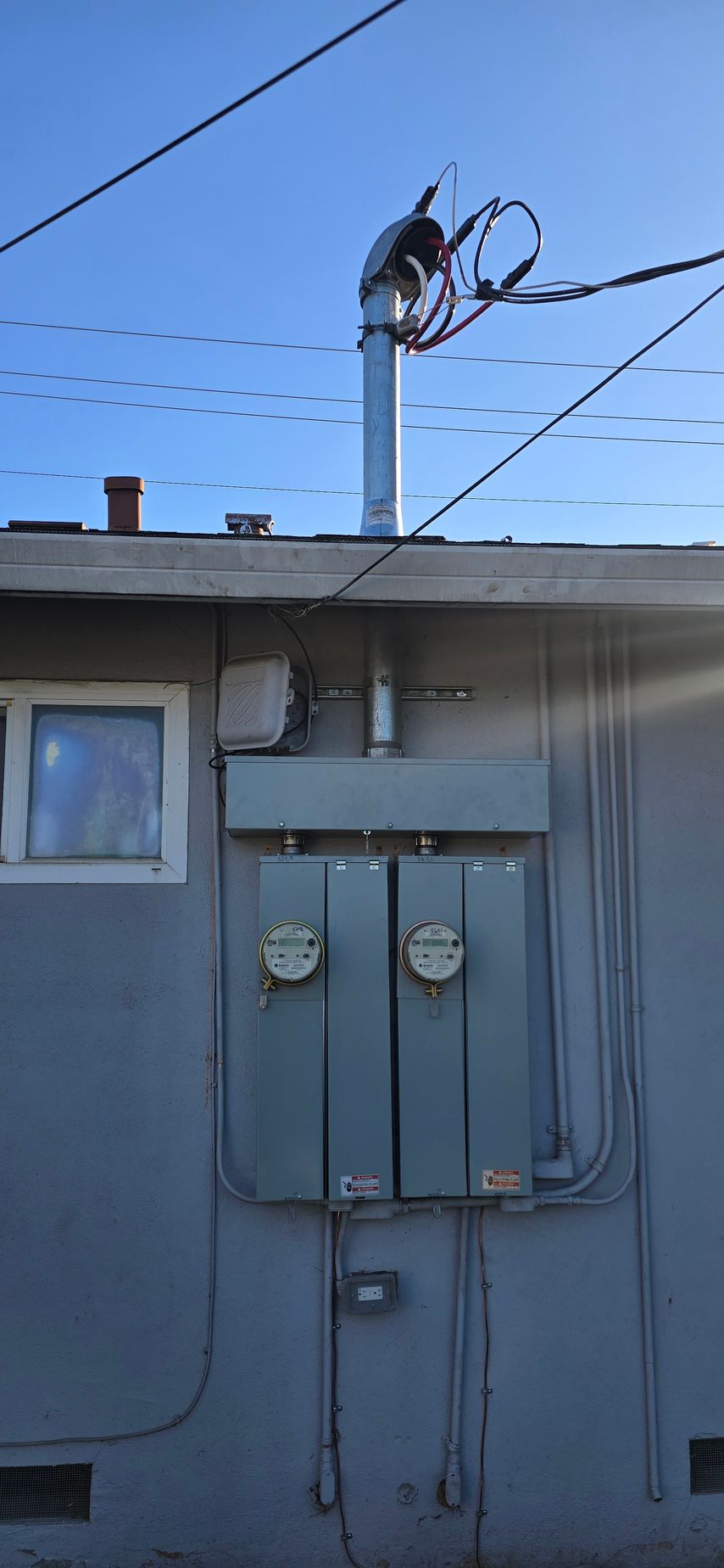 Utility meters on a house wall with rooftop power lines and a bird perched on the wires