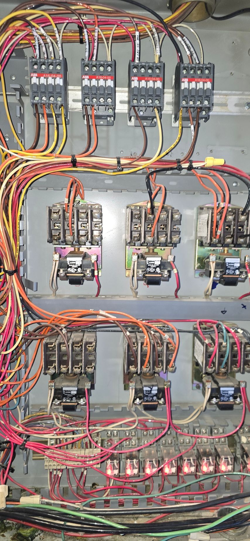 Electrical control panel with rows of relays, circuit breakers, and dense red, yellow, and orange wiring