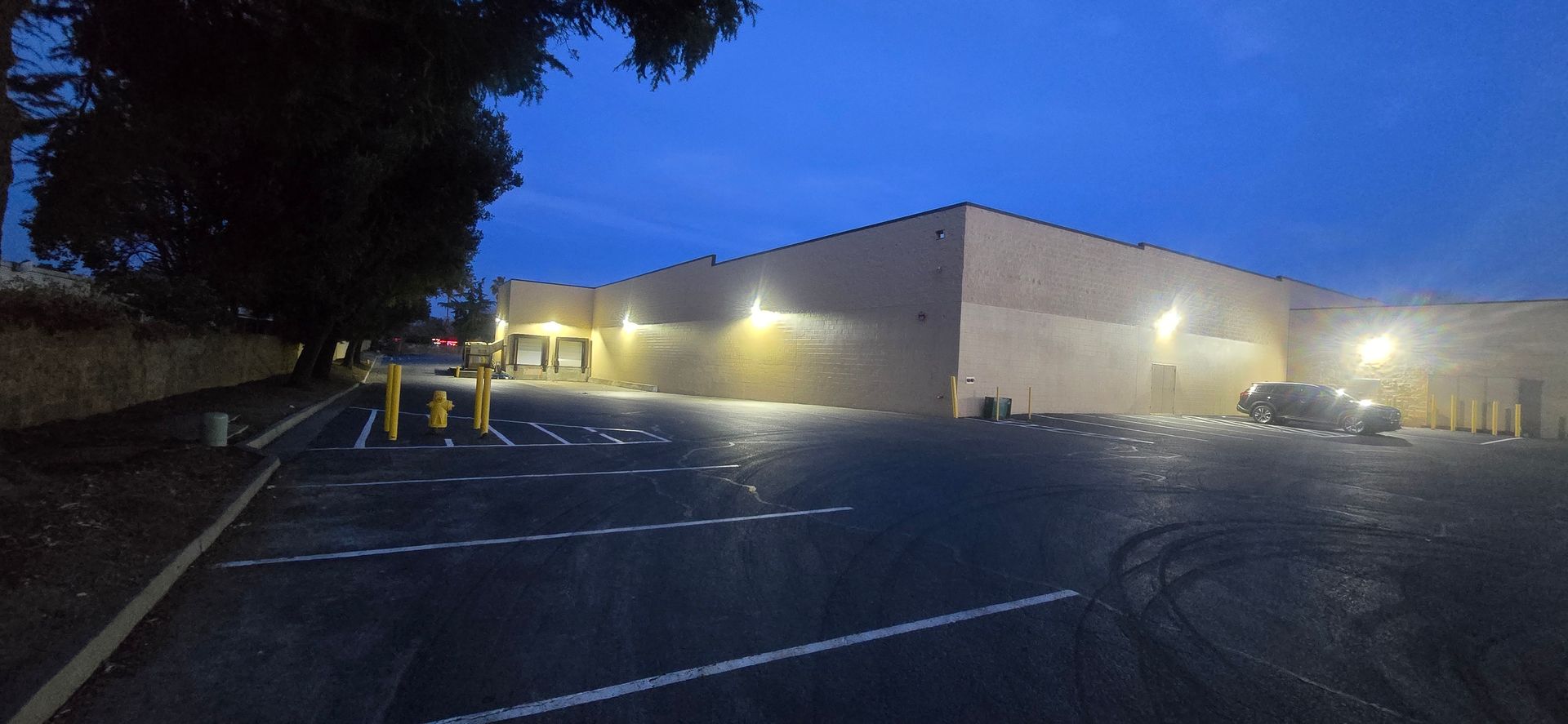 Large warehouse building at dusk with lit exterior lights and parking lot in front