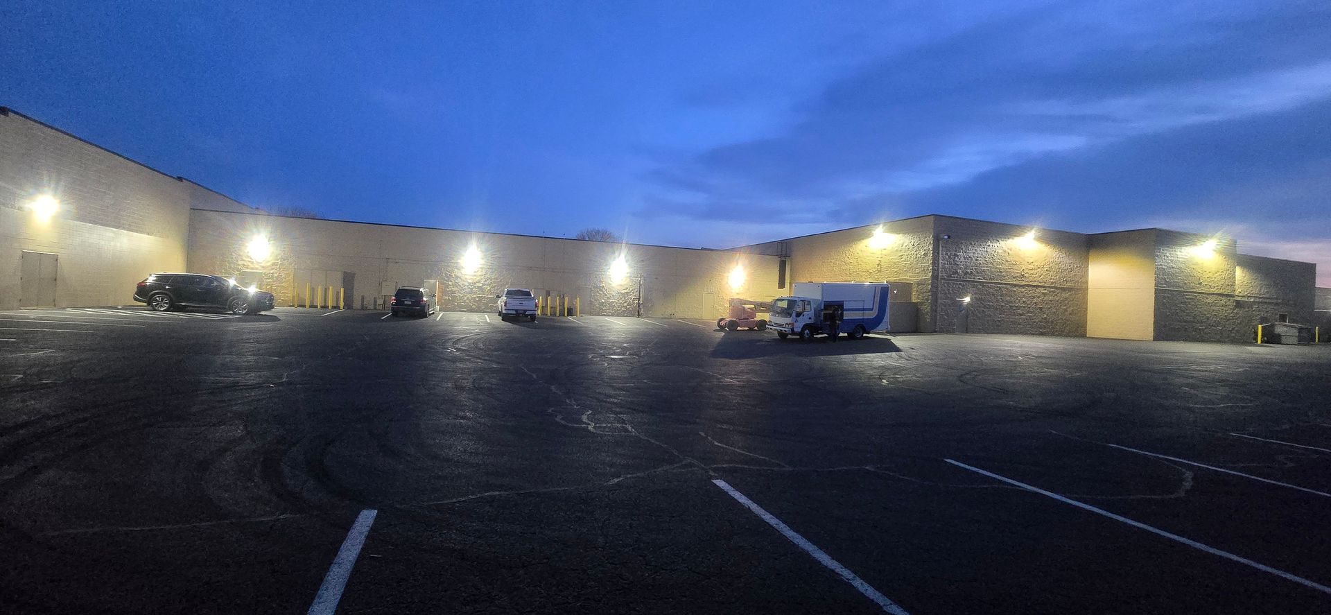 Snowy parking lot at night with lit building entrances and a few parked vehicles