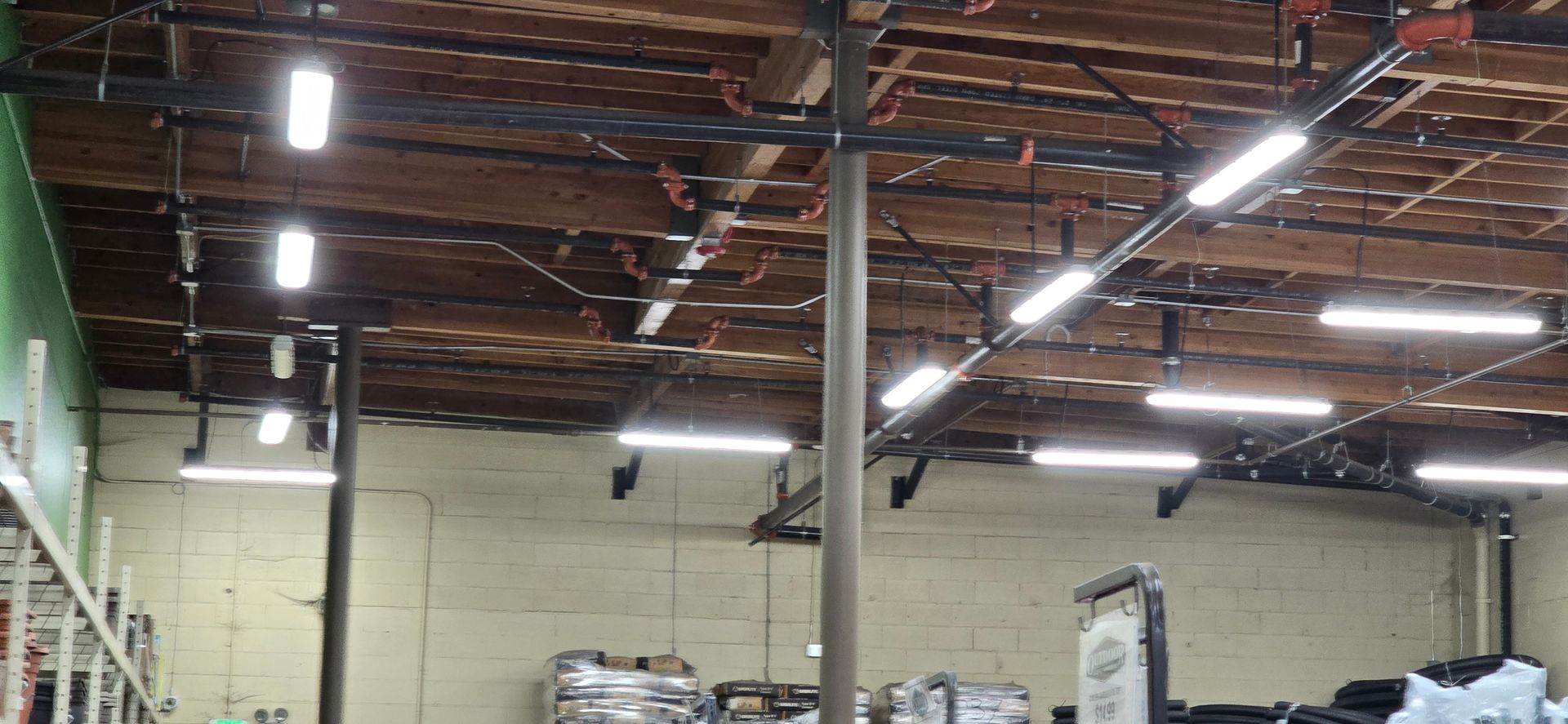 Warehouse interior with exposed ceiling beams, bright hanging lights, and stacked boxes below
