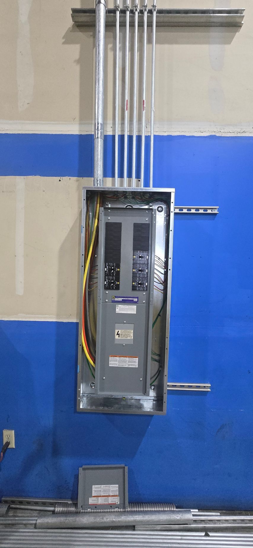 Electrical breaker panel with exposed wiring mounted on a blue-and-beige wall