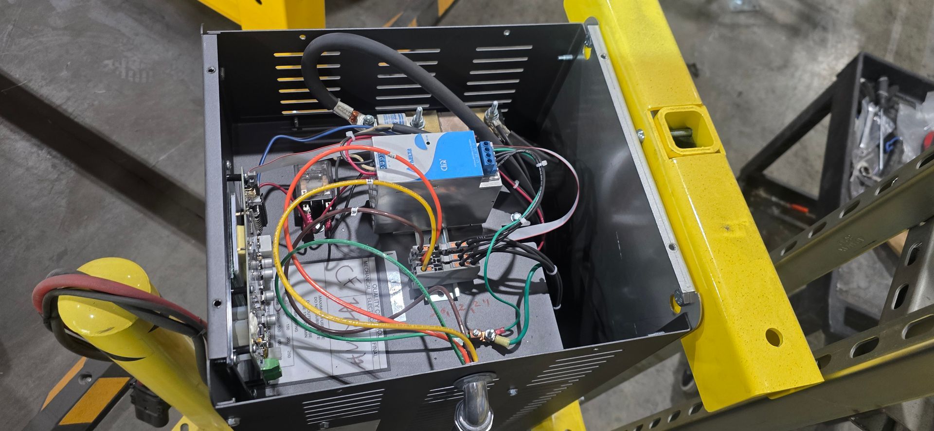Wiring-filled electronics box on a yellow industrial frame, viewed from above.