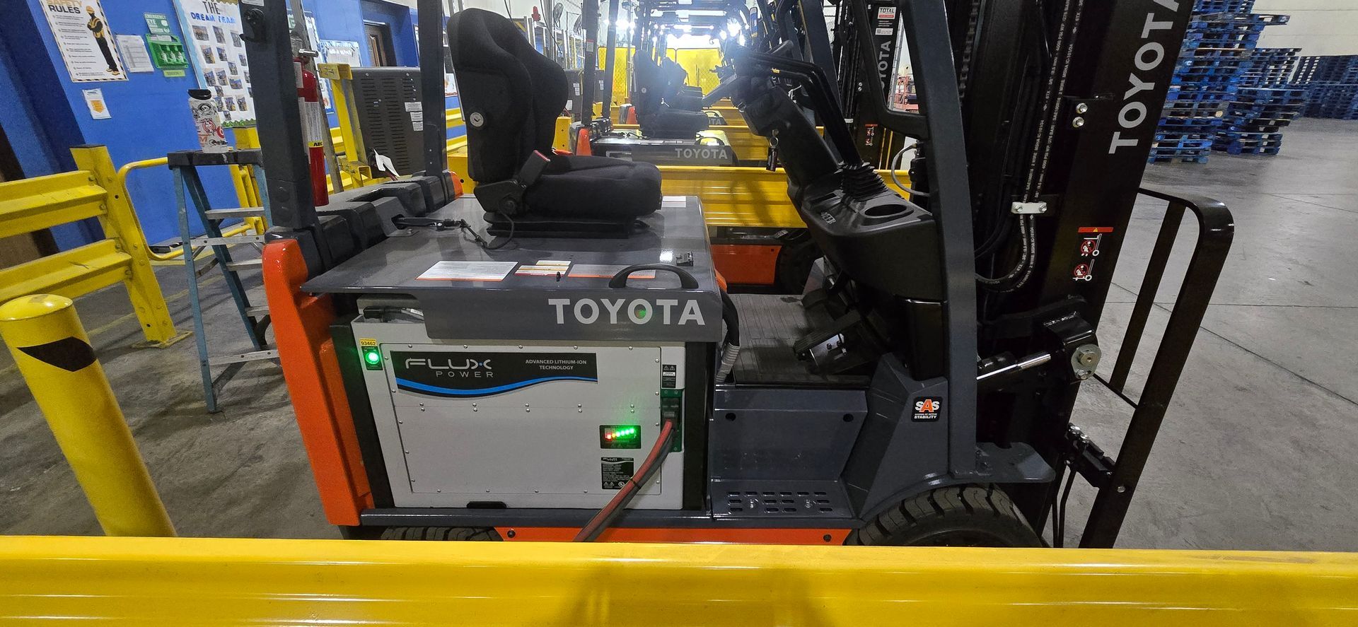 Toyota forklift in an industrial warehouse, with yellow safety rails and machinery in the background.