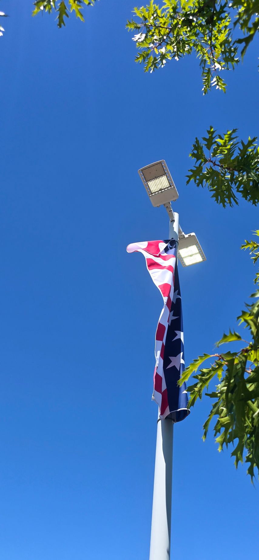 Tall pole with red, white, and blue banners beneath two streetlights against a clear blue sky.
