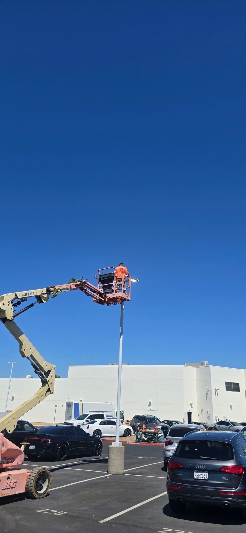 Worker in a cherry picker repairing a parking lot light pole under a clear blue sky.