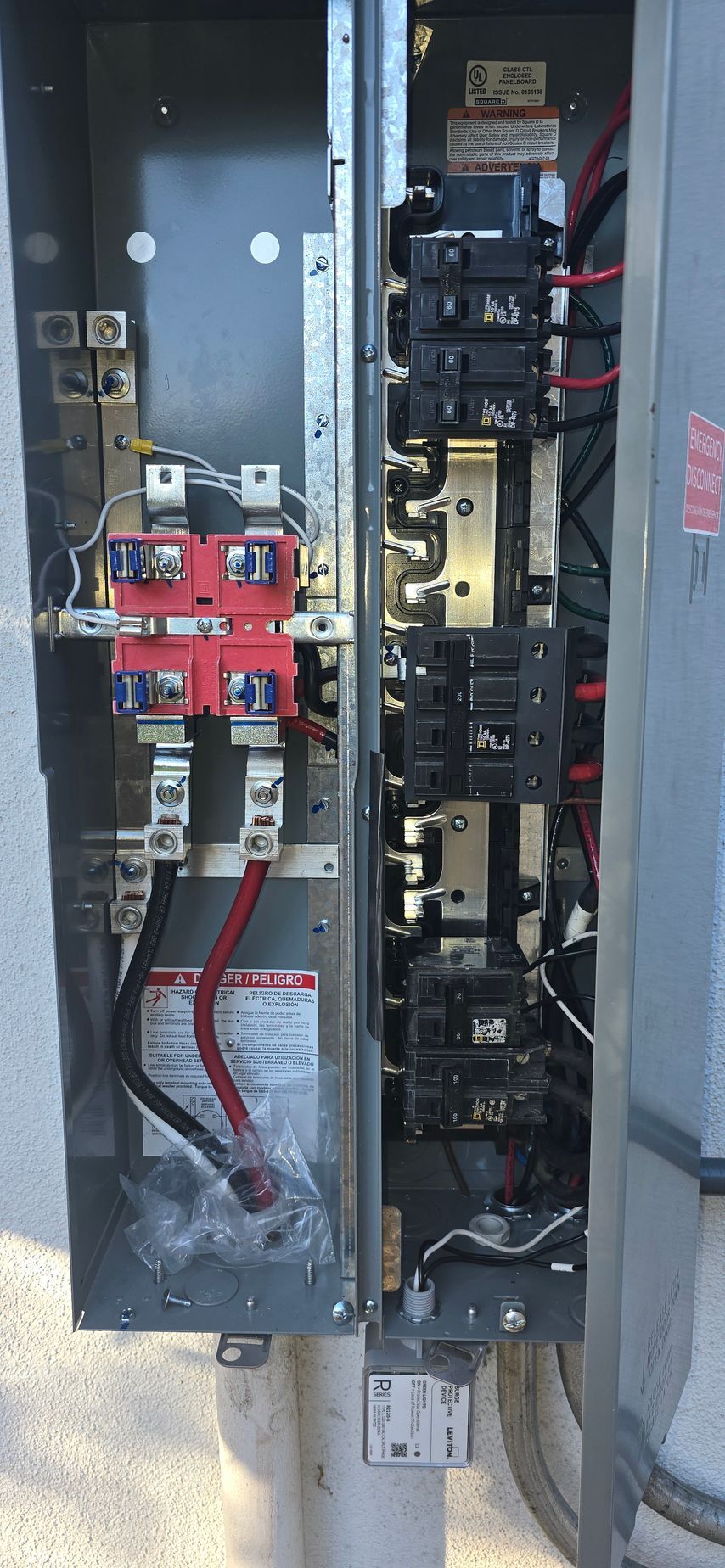 Open electrical panel with red and black circuit breakers and exposed wiring inside.