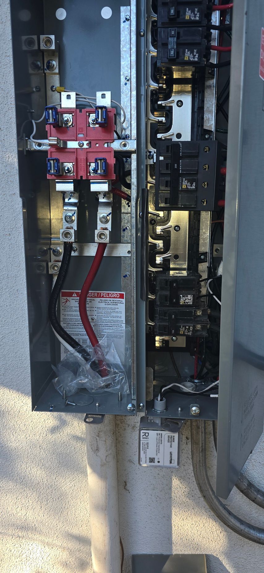 Open electrical breaker panel with red wiring and exposed components outdoors