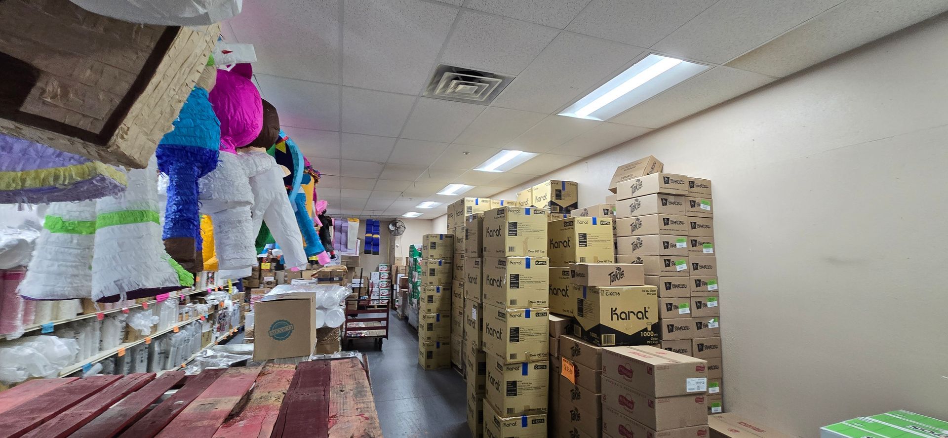 Stacked boxes line a narrow store aisle with colorful decorations hanging overhead.