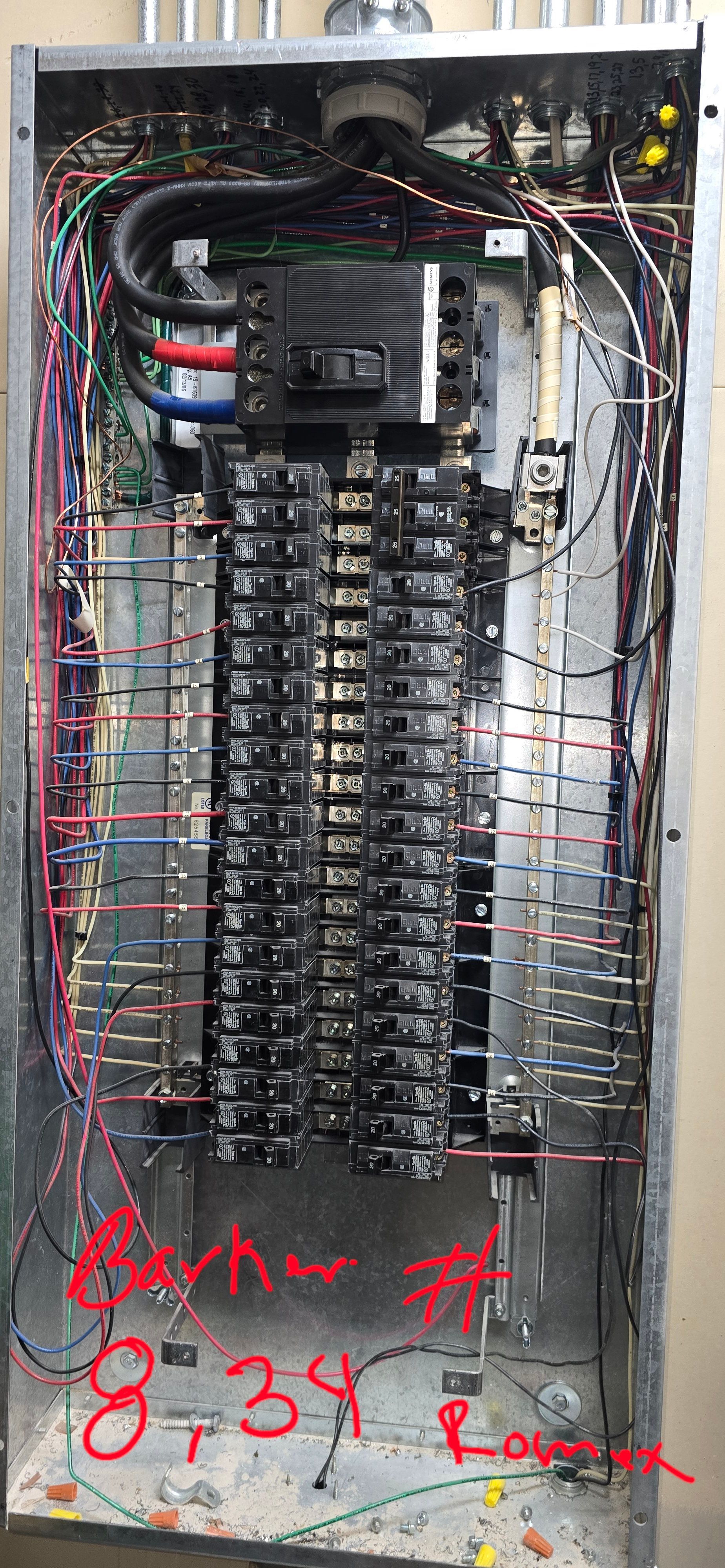 Open electrical breaker panel with many wires and handwritten red markings on the cover