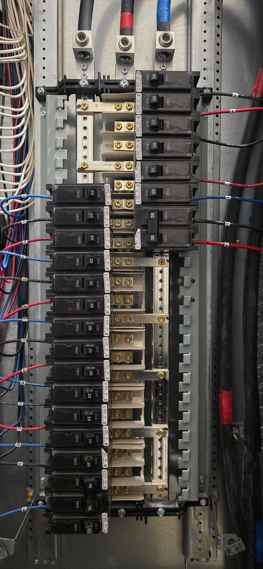 Electrical breaker panel with rows of black switches and colored wires inside a metal cabinet