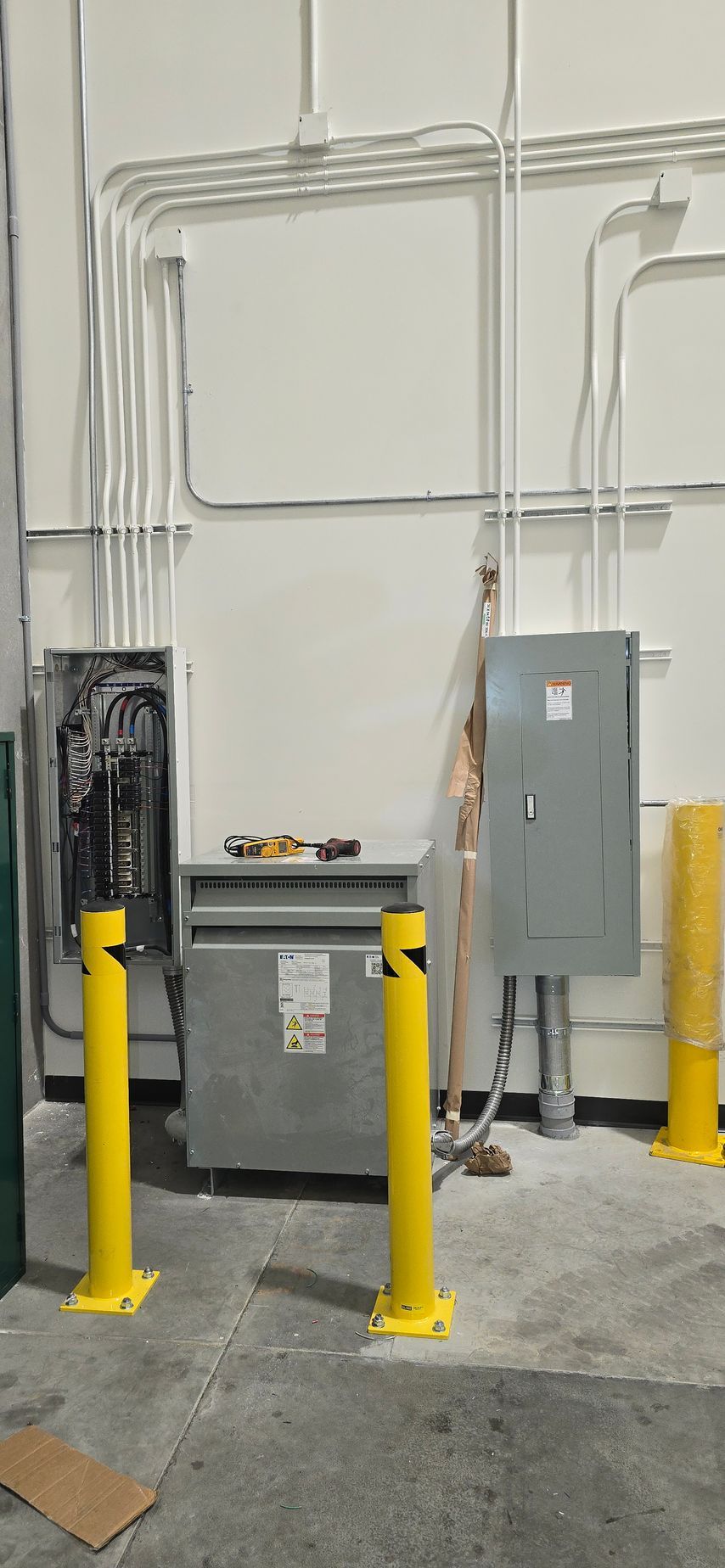 Industrial HVAC equipment and gray electrical cabinet with yellow safety bollards in a utility room