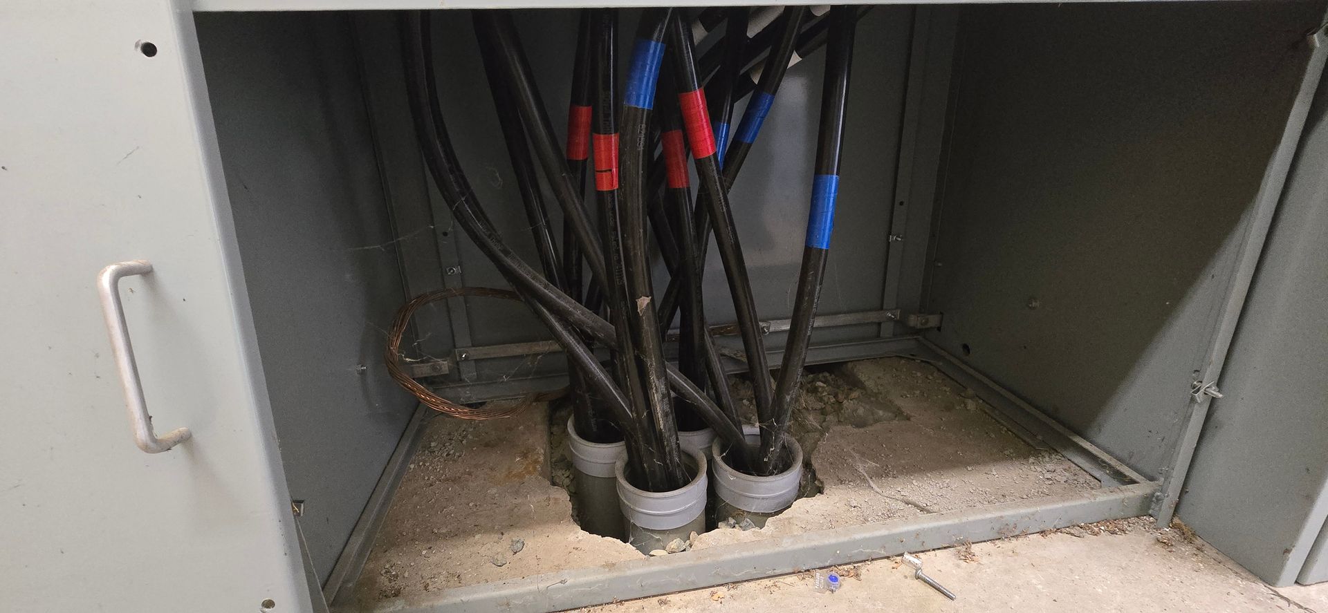 Open cabinet with bundled black cables entering through gray floor grommets