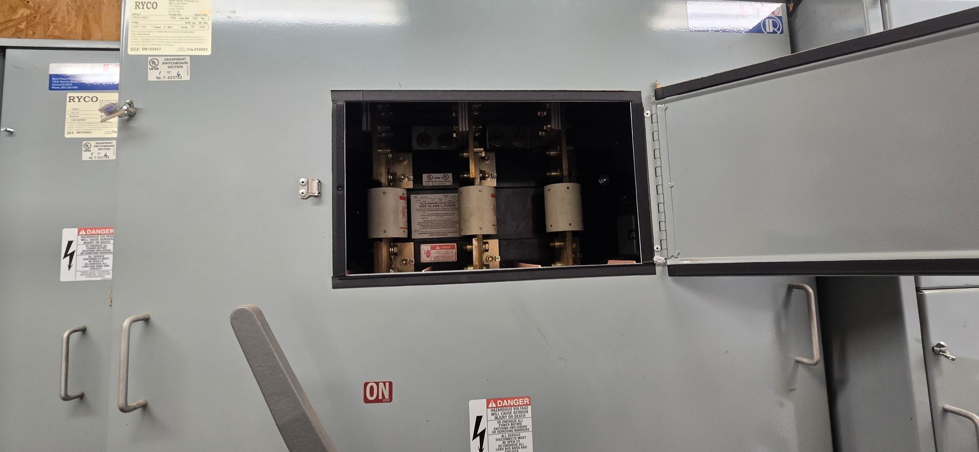 Open electrical panel with transformers inside a gray utility cabinet, door swung open