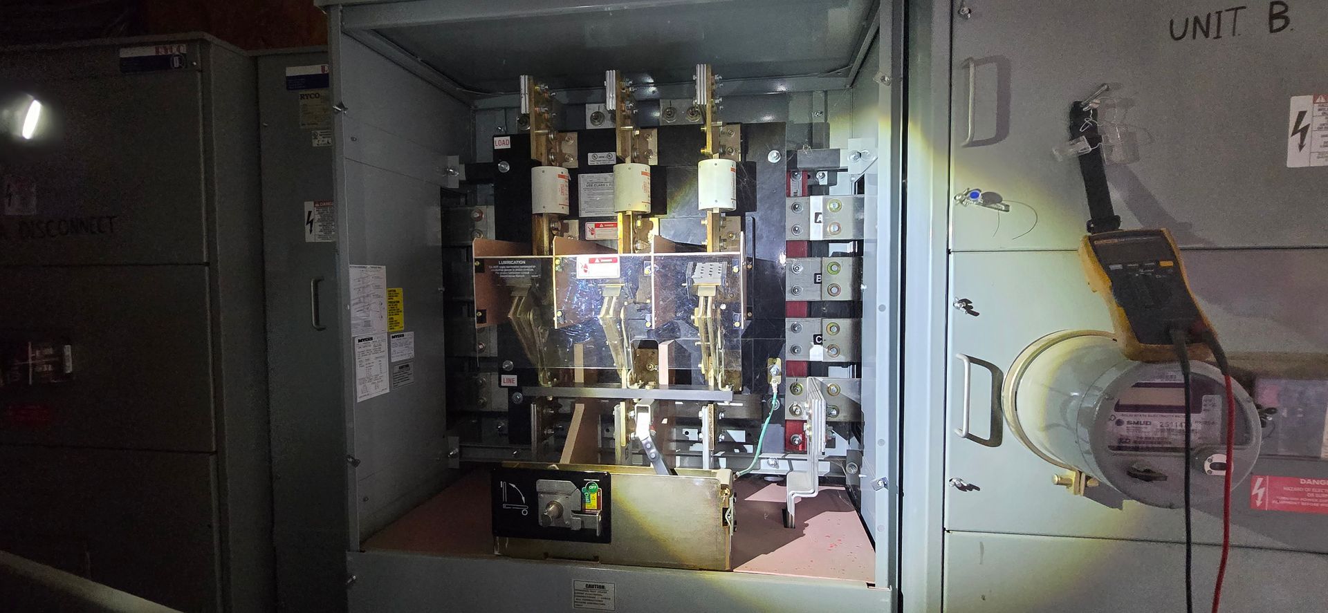 Industrial electrical control panel with wiring and illuminated components inside a dim utility room
