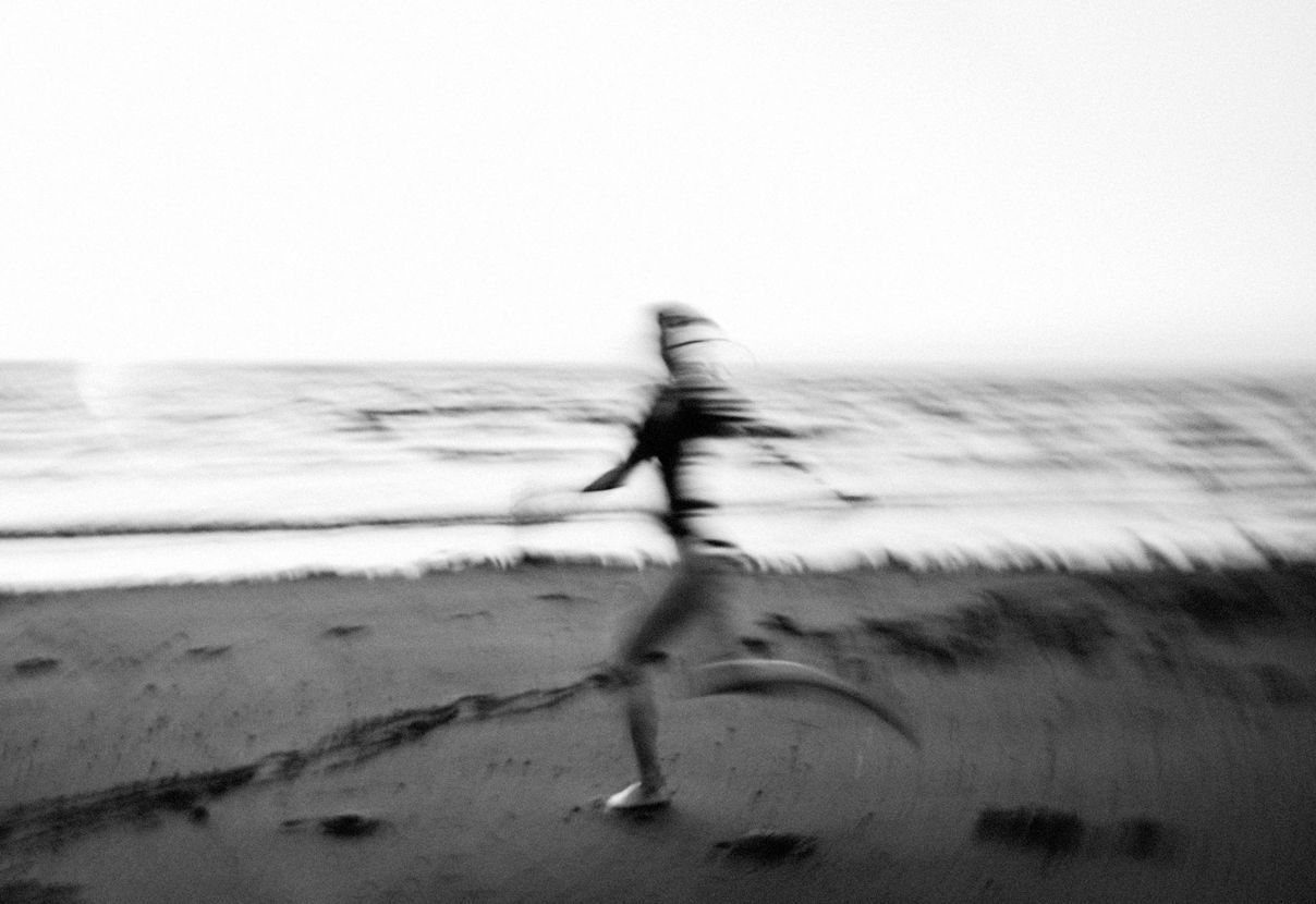 Blurred person running along a beach in black-and-white.