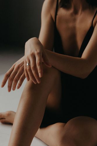 Person seated in a black bodysuit, resting crossed arms on one knee against a dark background