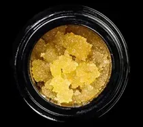 Close-up of yellow crystalline cannabis concentrate in a small black container
