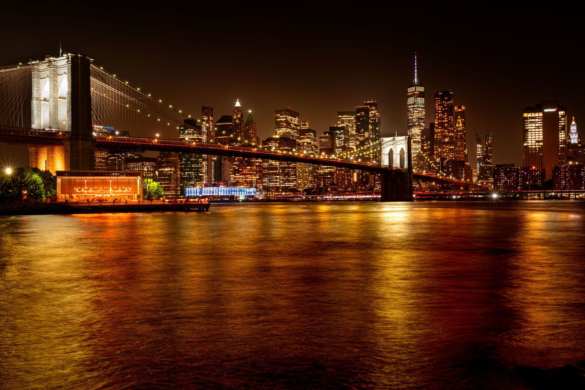 Night skyline with a lit suspension bridge reflecting golden lights on the water