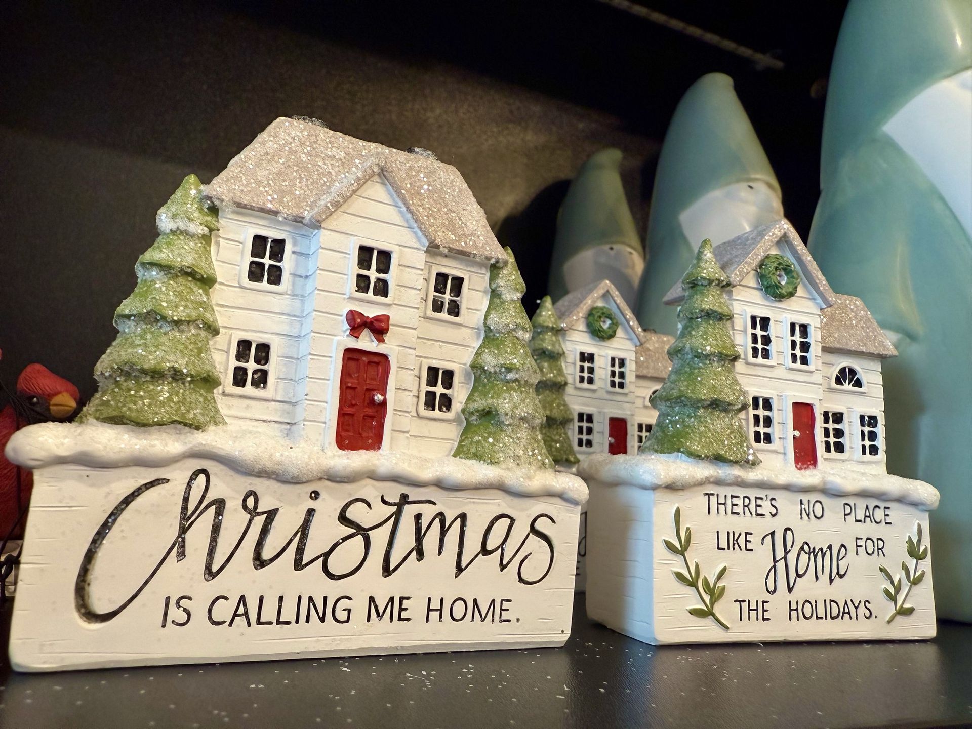Two christmas decorations on a shelf with one that says christmas is calling me home