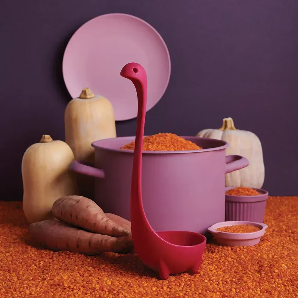 A pink ladle in the shape of a dinosaur is next to a pot of food