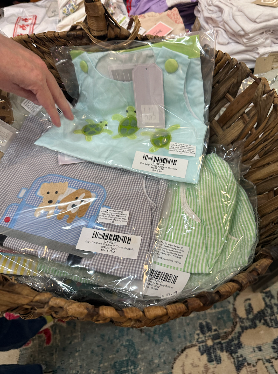 A person is holding a bag of baby clothes in a basket.
