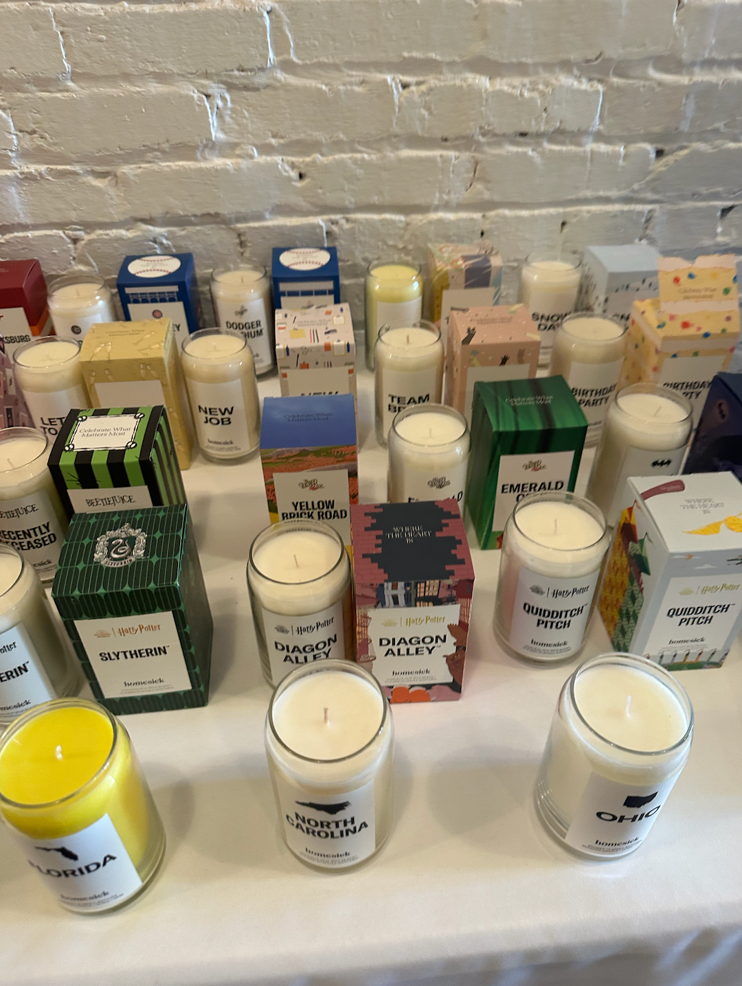 A bunch of candles are sitting on a table in front of a brick wall.