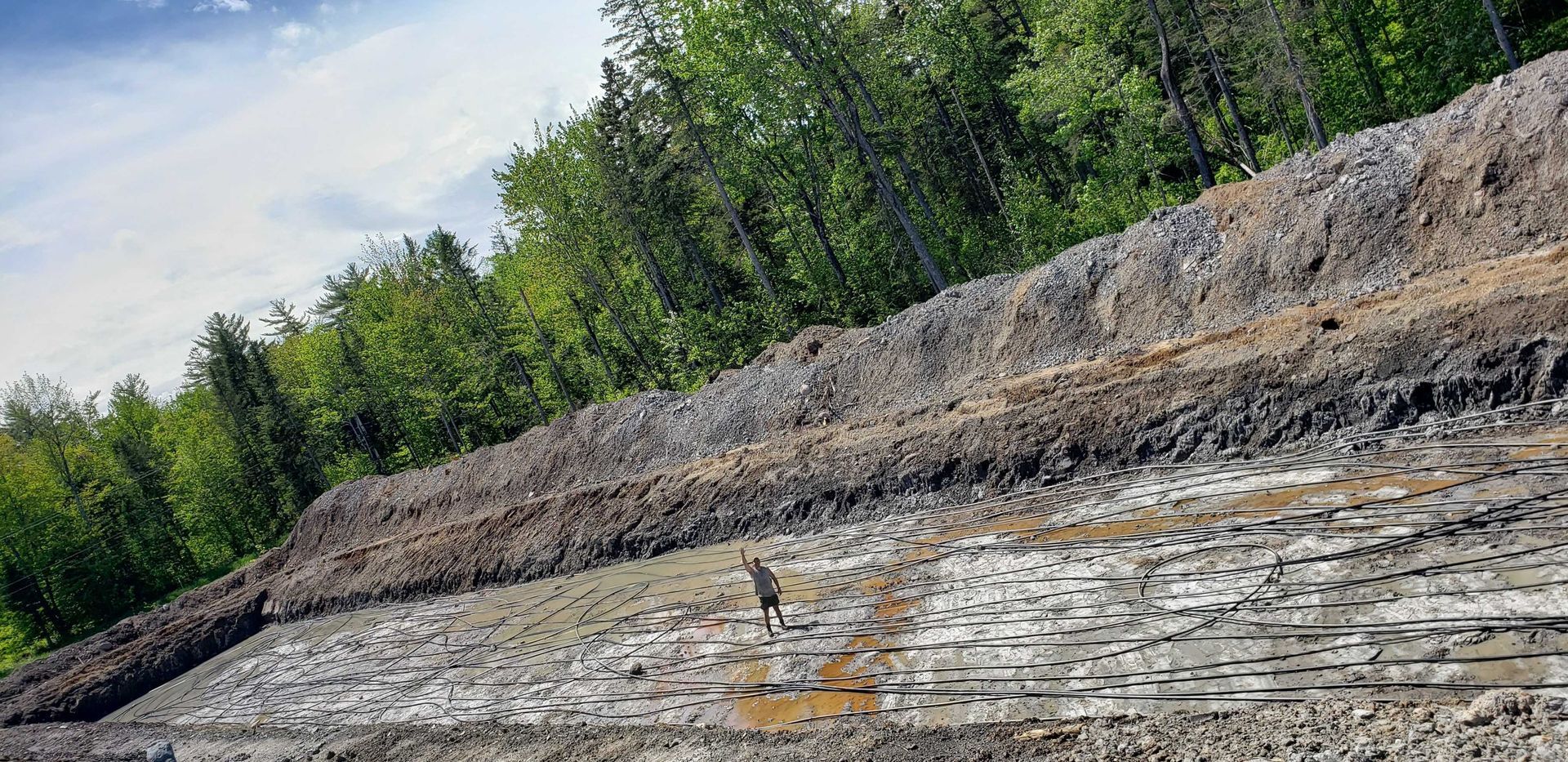 Talus rocheux en bord de route avec des arbres verts sous un ciel nuageux