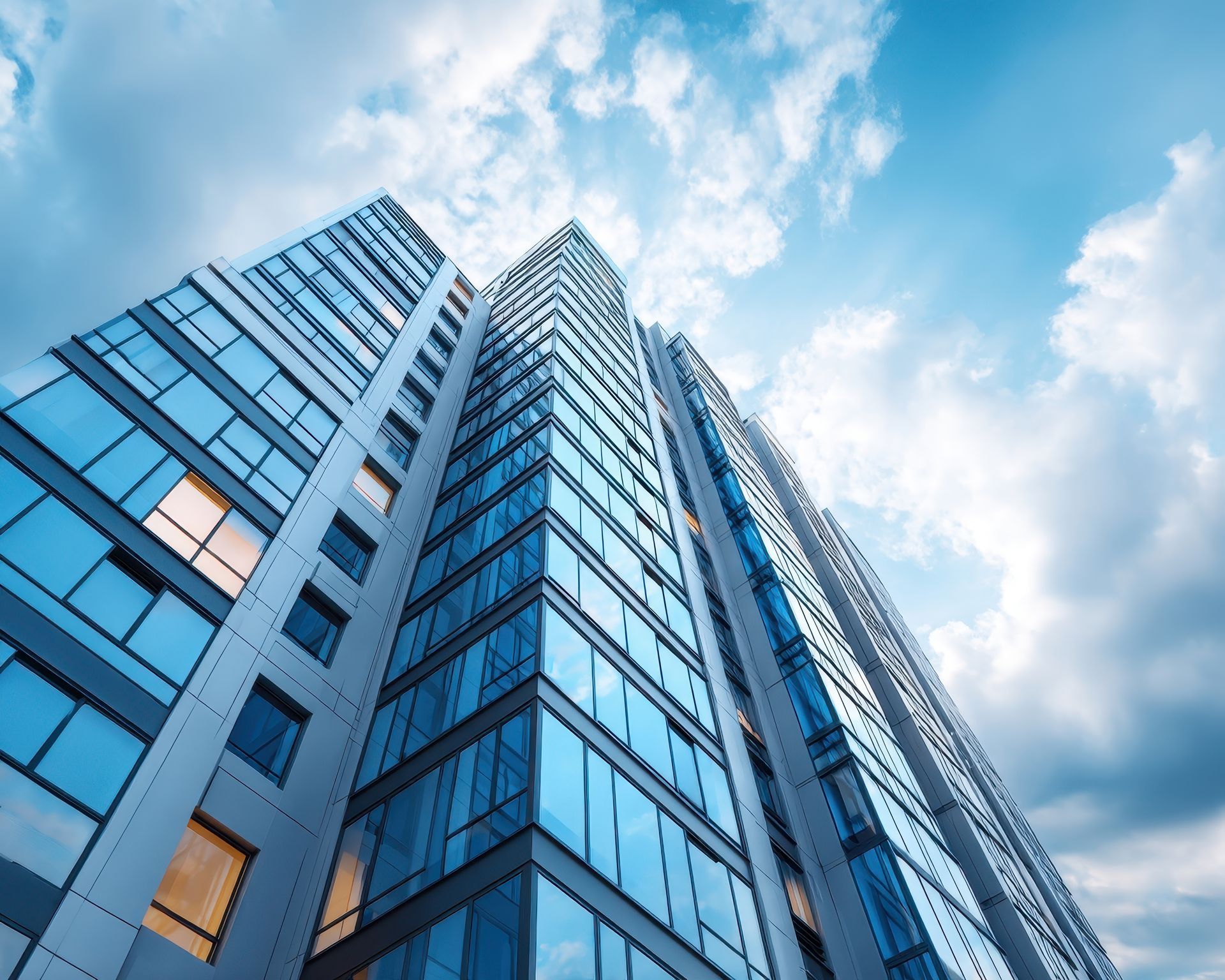 Vue en contre-plongée d'un immeuble d'appartements moderne en verre se détachant sur un ciel bleu nuageux.