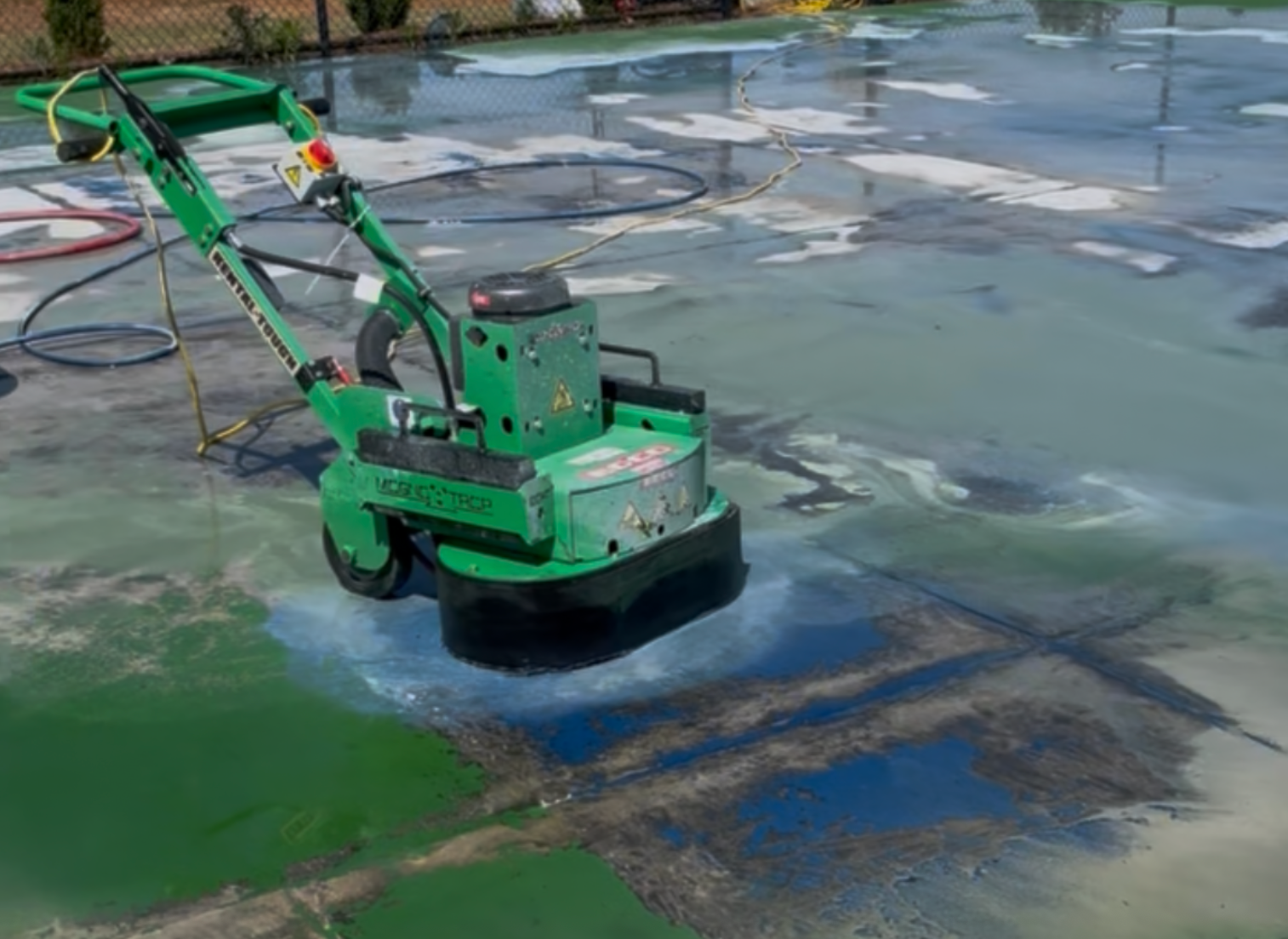 A green floor grinder machine smoothing a wet, messy concrete surface outdoors.
