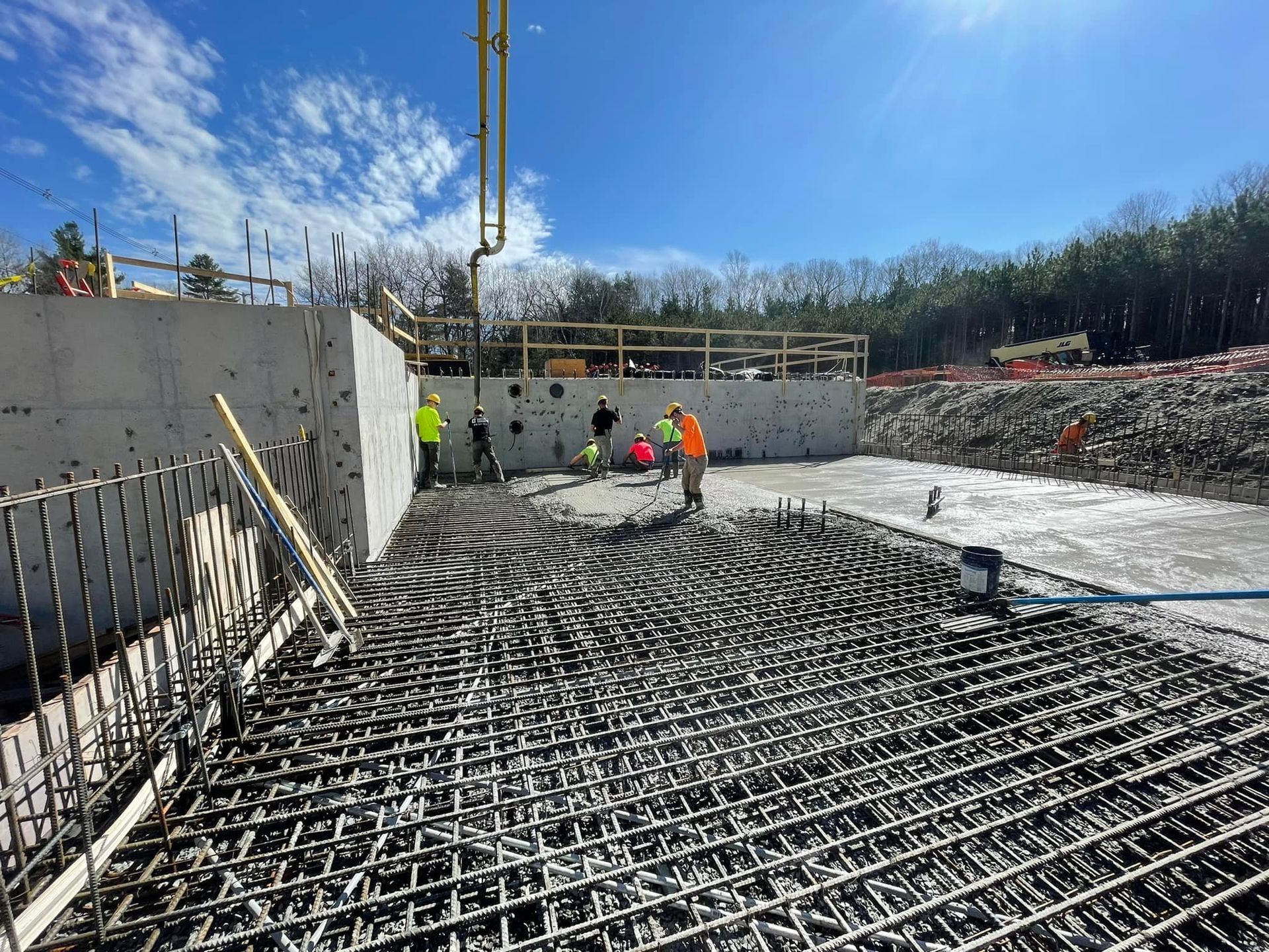 Construction workers pouring concrete on a foundation with rebar. Blue sky, sunny day.