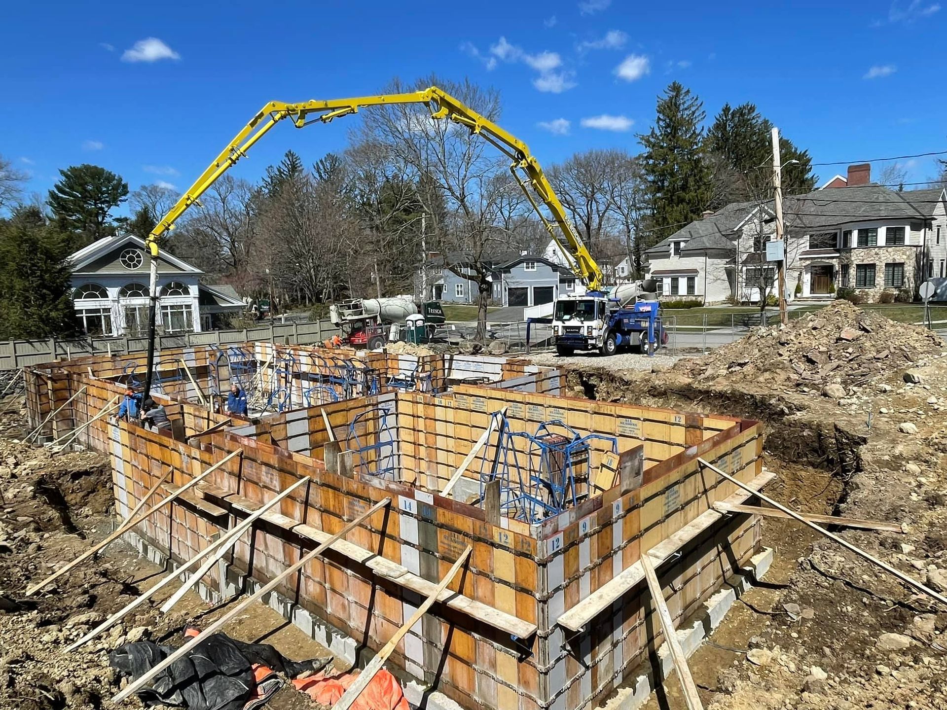 Construction site with concrete forms being filled by a pump truck under a blue sky.
