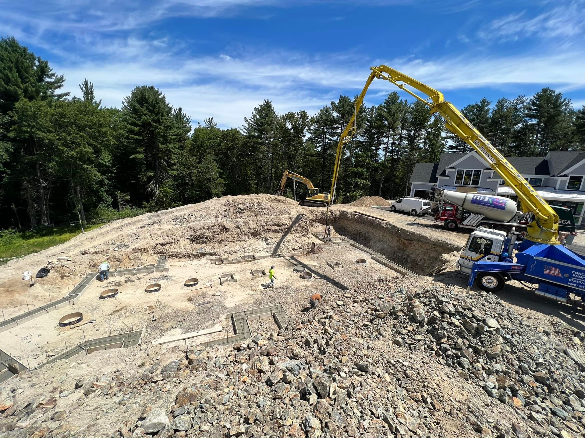 Construction site with concrete pump truck pouring concrete into foundation. Sunny day.
