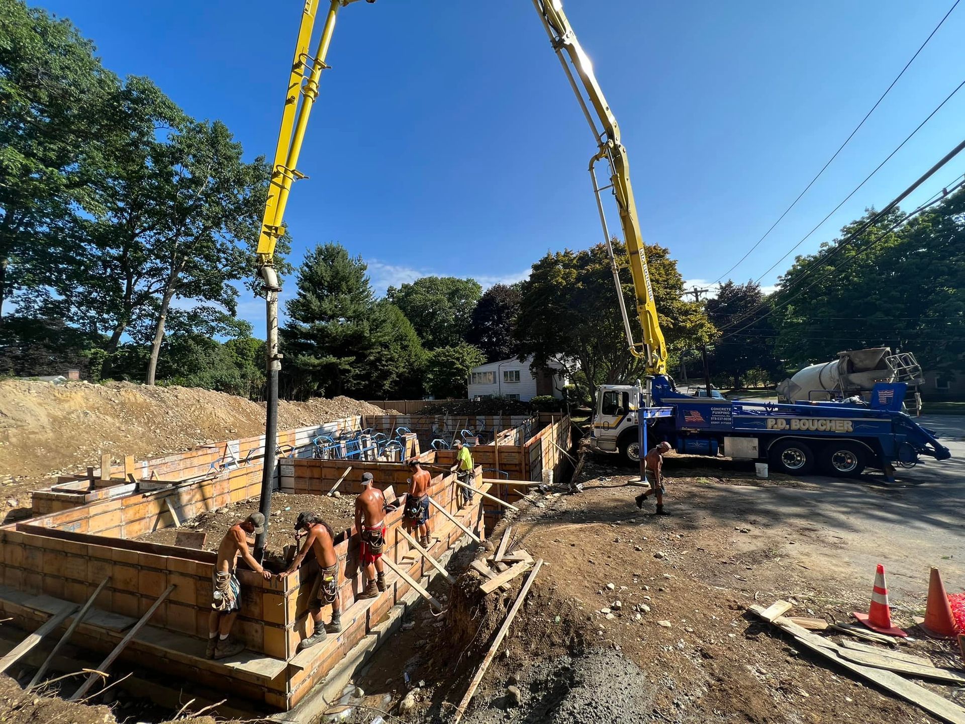 Construction site with workers pouring concrete into wooden forms with a pump truck. Blue sky.