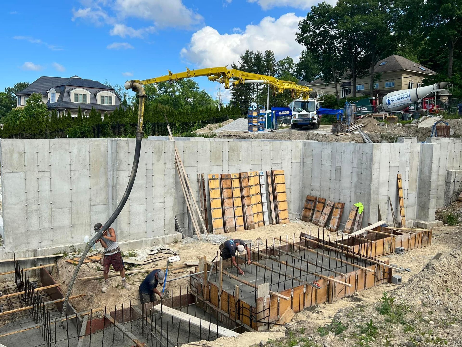 Construction site with workers pouring concrete into forms. A yellow boom truck is extending over the work.