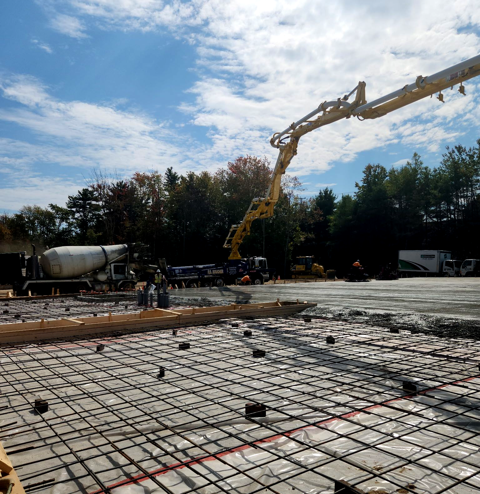 Construction site with concrete being poured by a pump truck onto a rebar grid.