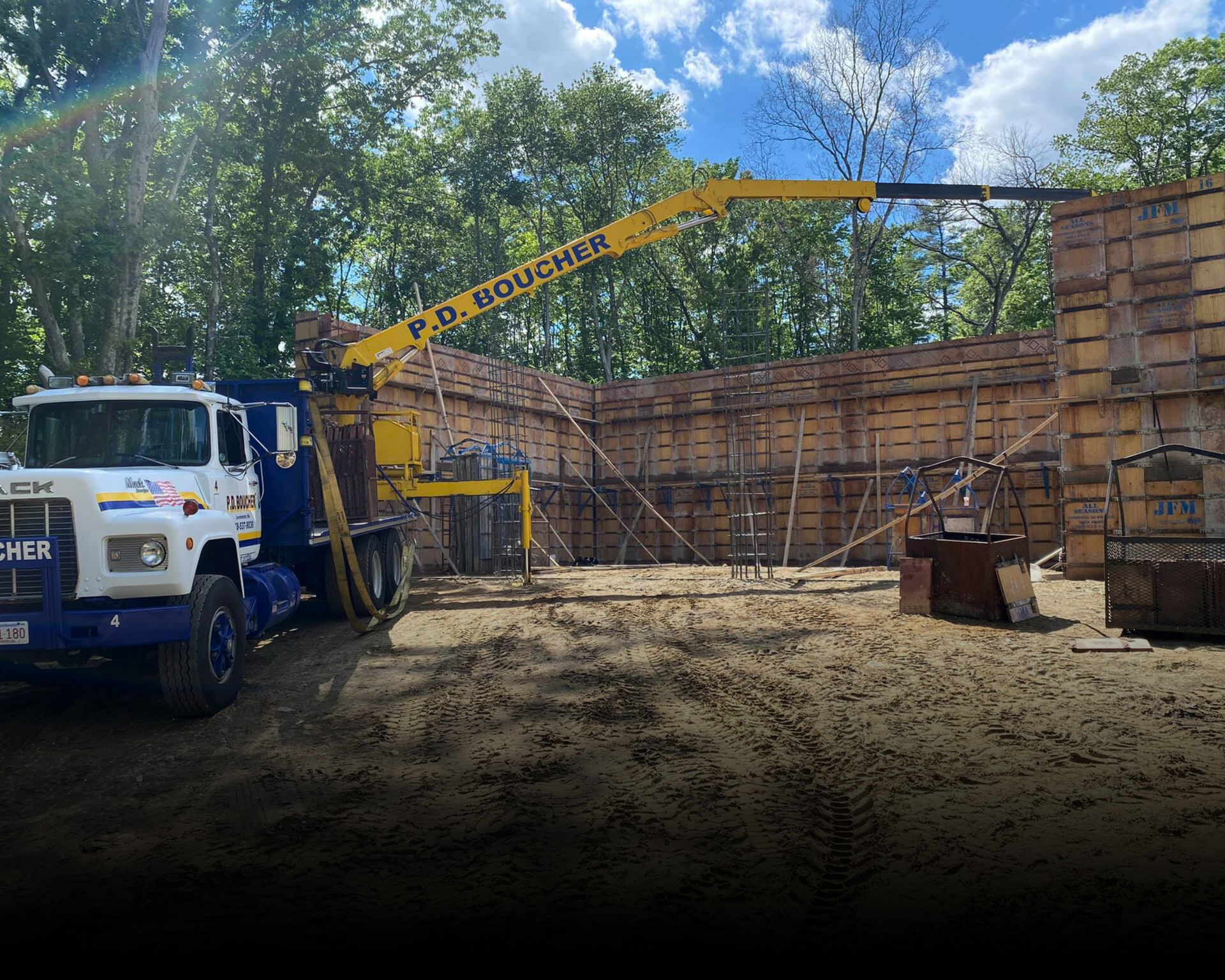 Construction site with a truck-mounted crane lifting materials. Wooden forms for concrete walls are visible.