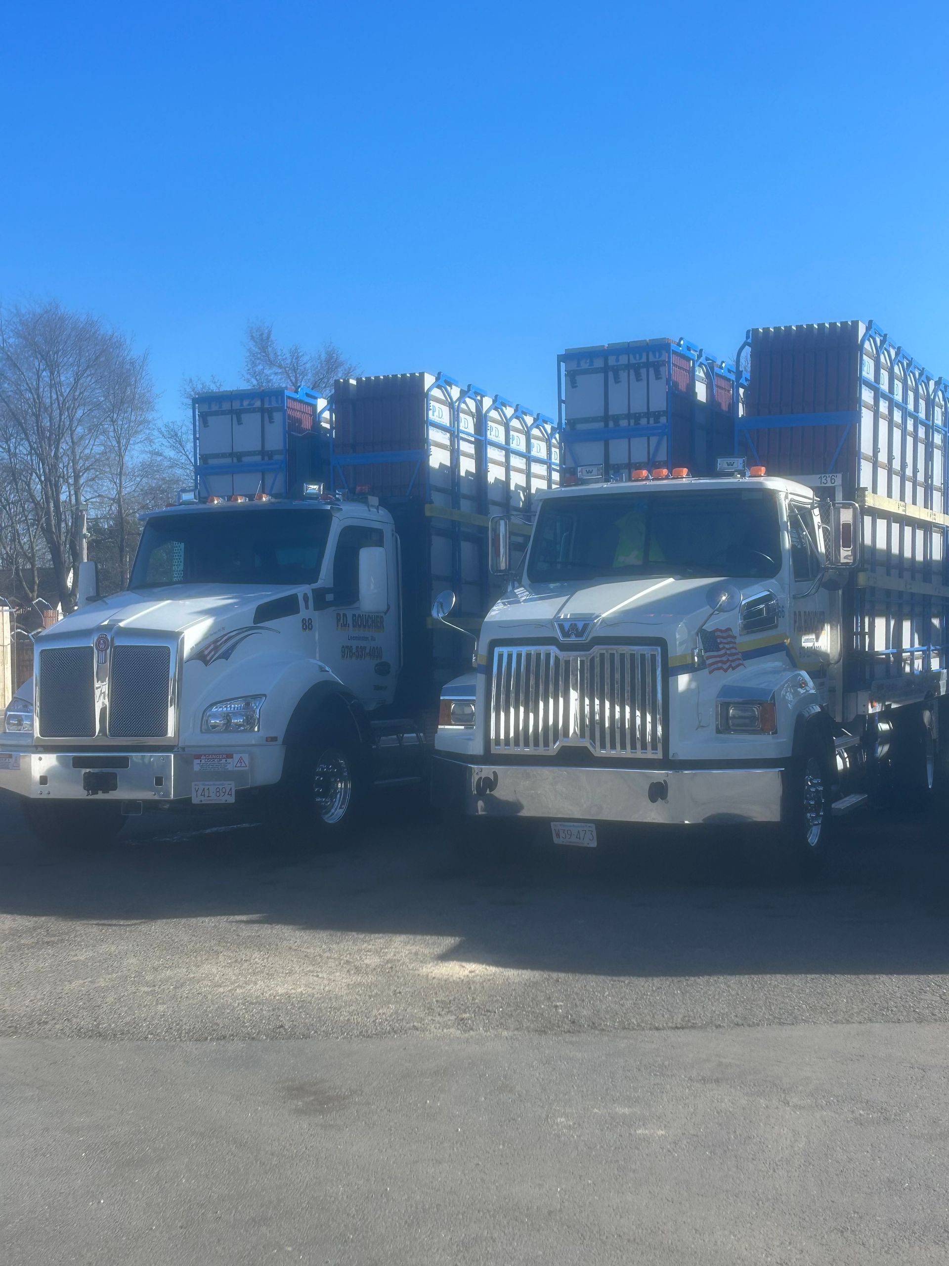 Two white semi-trucks loaded with stacked containers on a clear, sunny day.